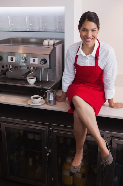 Jolie barista, souriant à la caméra, assis sur le comptoir