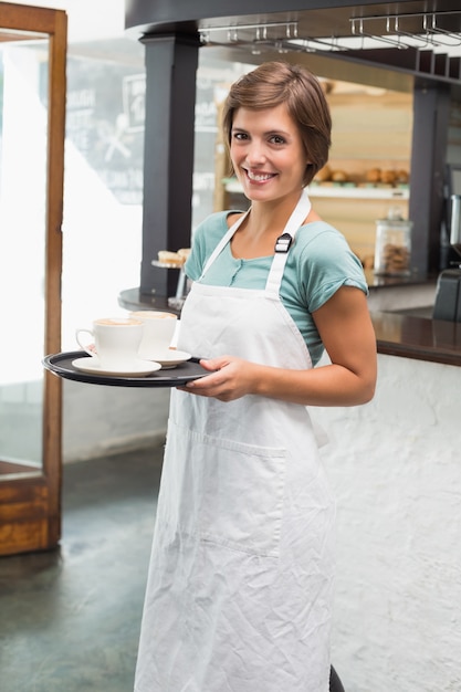 Jolie barista souriant à la caméra tenant le plateau