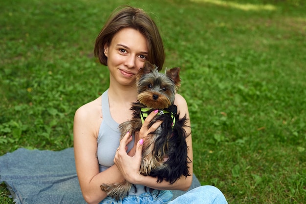 Jolie belle femme avec petit Yorkshire Terrier dans un parc à l'extérieur. Portrait de mode de vie.