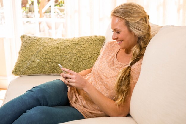 Jolie blonde à l'aide d'un smartphone sur le canapé du salon