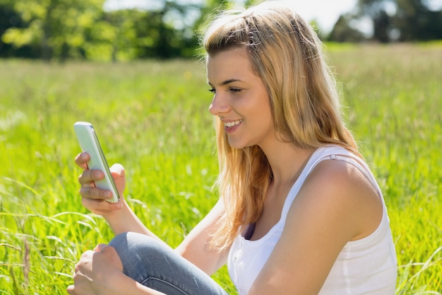 Jolie blonde assise sur l&#39;herbe envoyant un texte