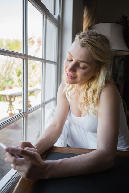 Jolie blonde assise près de la fenêtre en envoyant un texte