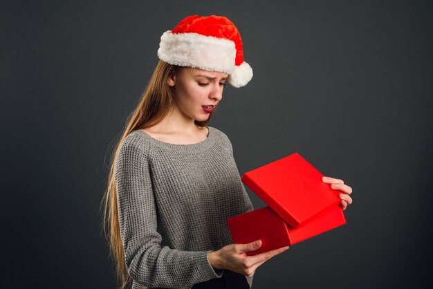 La jolie blonde au chapeau du père Noël ouvre un cadeau du nouvel an rouge pour Noël.