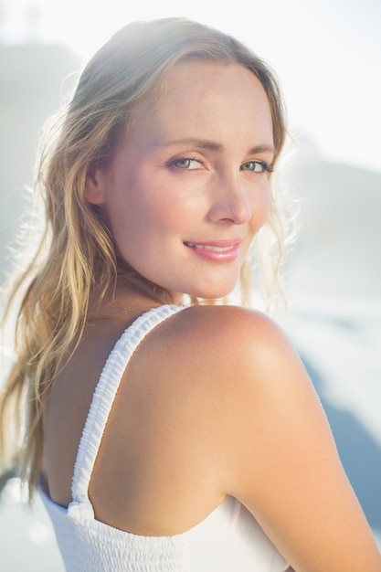 Jolie blonde debout sur la plage en robe blanche