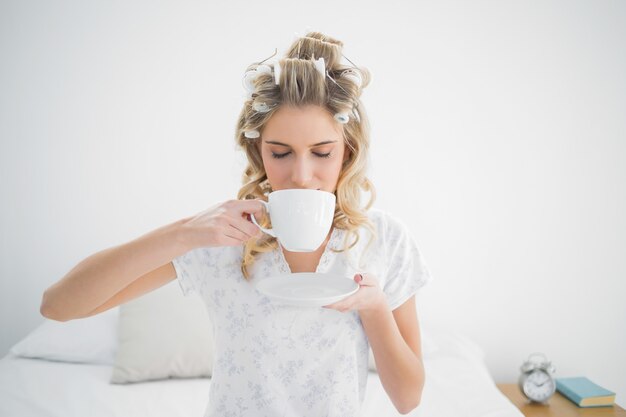 Jolie blonde détendue portant des bigoudis boire du café