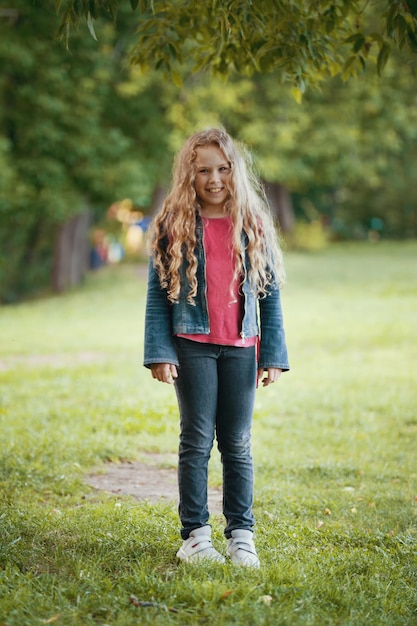 Jolie blonde enfant souriant portant une veste en jean dans le parc