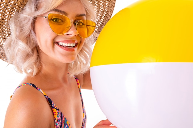 Jolie blonde femme caucasienne se dresse en maillot de bain avec grande plage de caoutchouc balle colorée et sourires isolés