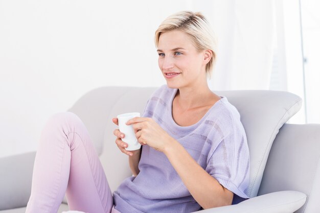 Jolie blonde femme se détendre sur le canapé et tenant une tasse