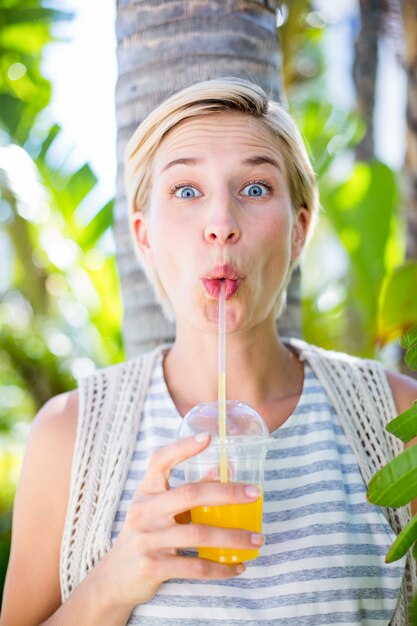 Jolie blonde femme souriante à la caméra et boire du jus d&#39;orange