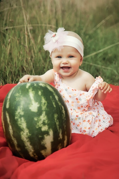 Jolie blonde heureuse aux yeux bleus fille de 8 mois dans l'herbe avec pastèque