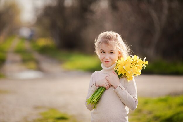 Jolie blonde heureuse petite fille avec des jonquilles jaunes au pays du printemps