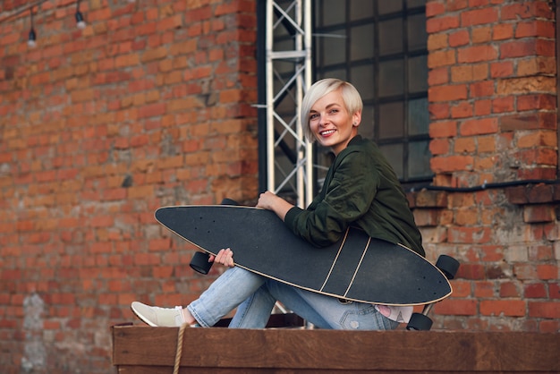 Jolie blonde avec longboard au mur de briques.