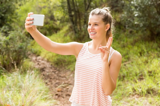 Jolie blonde montrant le signe de la paix et de prendre des selfies