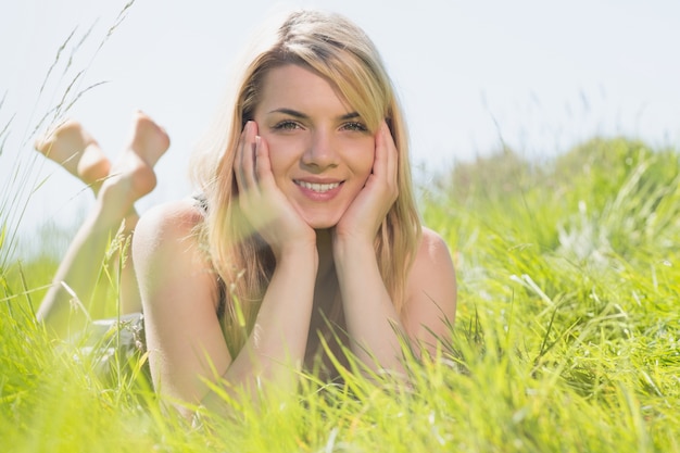 Jolie blonde en robe d&#39;été allongée sur l&#39;herbe, souriant à la caméra