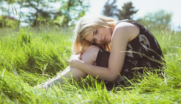 Jolie blonde en robe d&#39;été assis sur l&#39;herbe