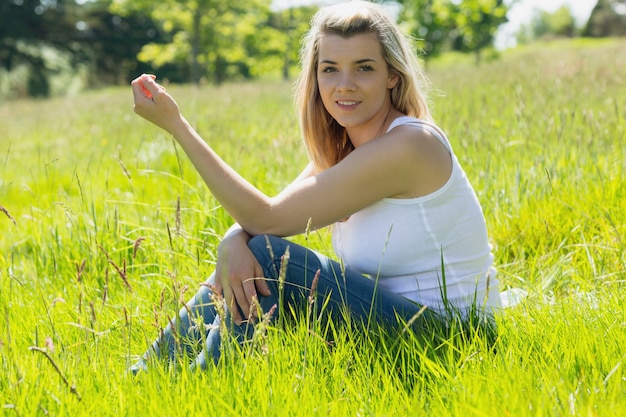 Jolie blonde, souriant à la caméra, assis sur l&#39;herbe