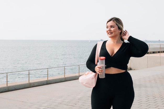 Jolie blonde taille plus fille marchant avec des vêtements de sport et une bouteille d'eau après l'exercice