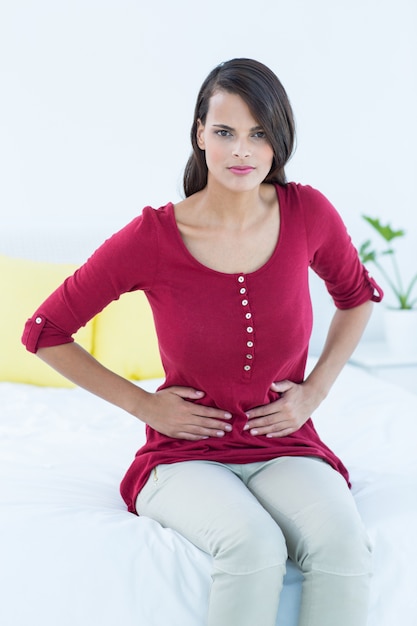 Photo jolie brune assise sur le lit avec douleur à l'estomac