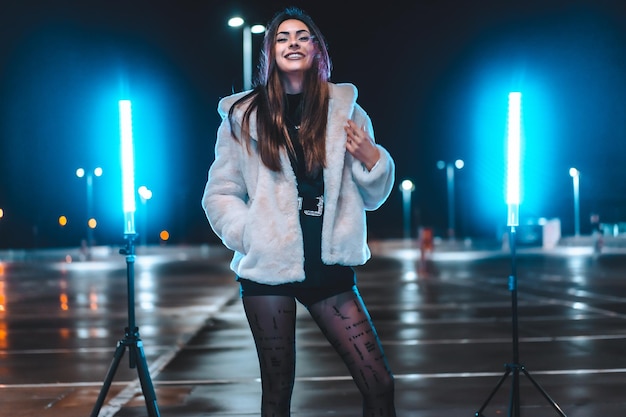 Jolie brune caucasienne dans une veste en laine rose dans un parking vide illuminé