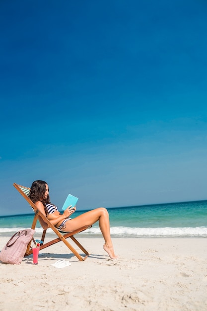 Jolie brune en lisant un livre sur une chaise longue