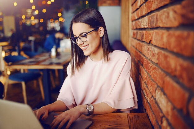 Jolie brune avec des lunettes à l'aide d'un ordinateur portable assis dans une cafétéria