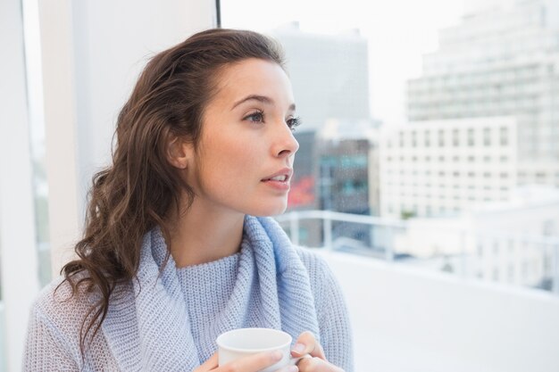 Jolie brune prenant un café près de la fenêtre