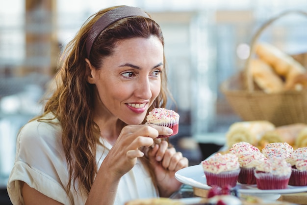 Jolie brune tenant et sentant un petit gâteau dans la boulangerie