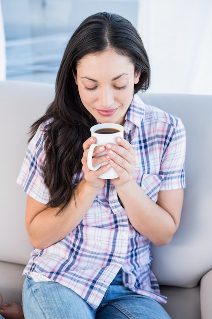 Jolie brune tenant une tasse de café sur le canapé