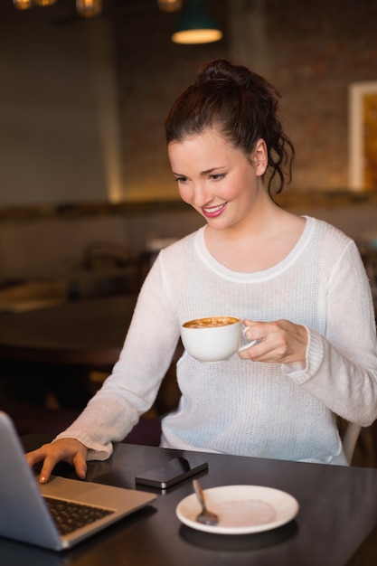 Jolie brunette prenant un café en utilisant un ordinateur portable au café