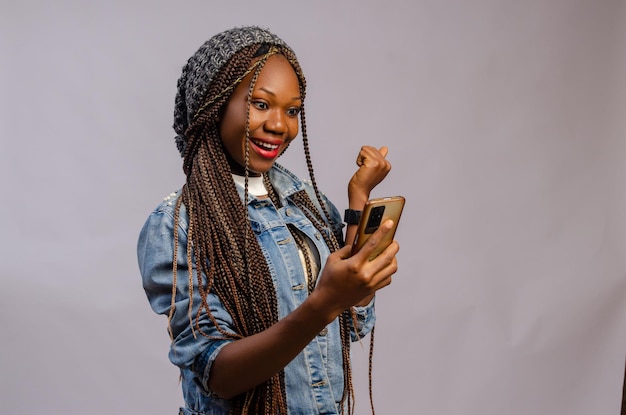 Jolie dame africaine portant un tissu décontracté se sentant excitée par ce qu'elle a vu sur son téléphone