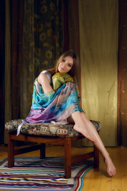 Jolie dame en foulard de soie autour de sa tête posant sur un canapé avec un tissu coloré