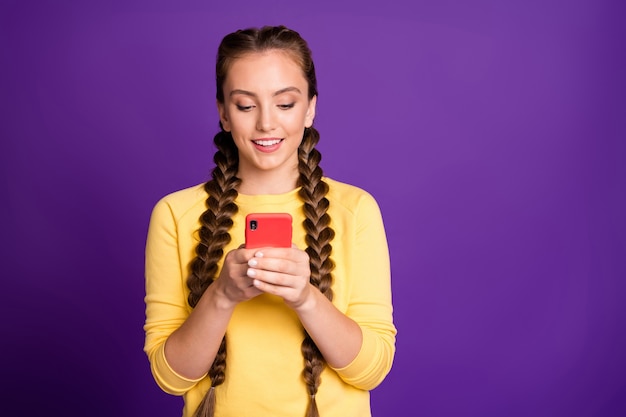 Jolie dame longues tresses tenant la main du téléphone la lecture de nouveaux commentaires positifs porter décontracté jaune pull pantalon rouge isolé mur de couleur pourpre