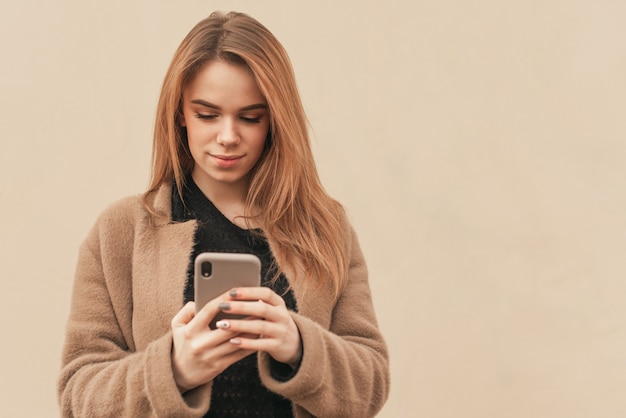 Jolie dame avec smartphone en mains sur fond beige.