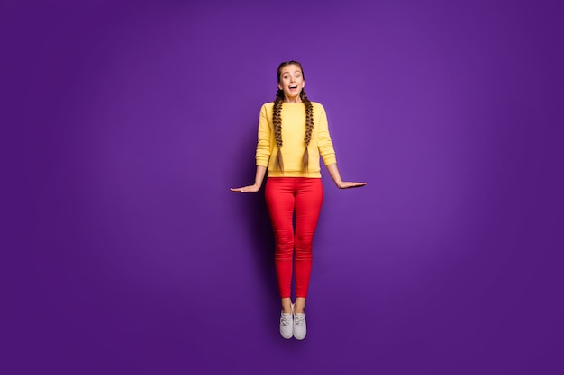 Jolie dame teen pleine longueur sautant haut s'amusant personne timide porter décontracté jaune pull pantalon rouge isolé mur de couleur violet vif