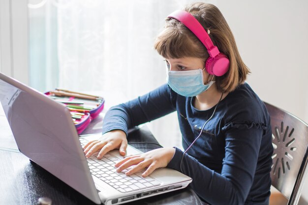 Jolie écolière étudie les devoirs pendant sa leçon en ligne à la maison, la distance sociale pendant la quarantaine,