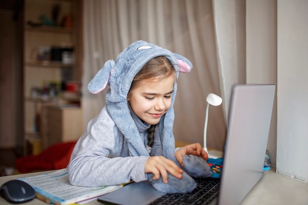 Jolie écolière portant un chapeau de lapin drôle avec des oreilles pendant la leçon en ligne ennuyeuse