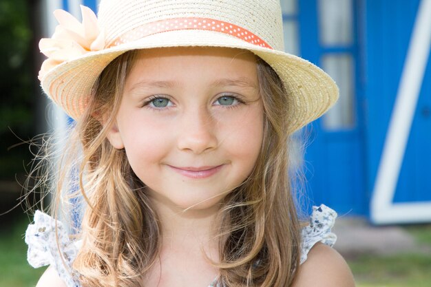 Jolie enfant fille avec chapeau de paille devant maison bleue en bois jour de printemps