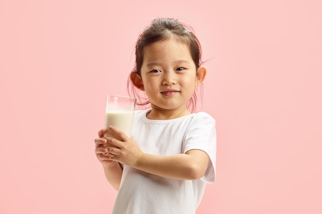 Une jolie enfant tenant un verre de lait sur un isolé rose