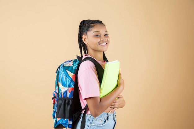 Jolie étudiante afro-américaine de retour au lycée, avec cahier et sac à dos, fond jaune