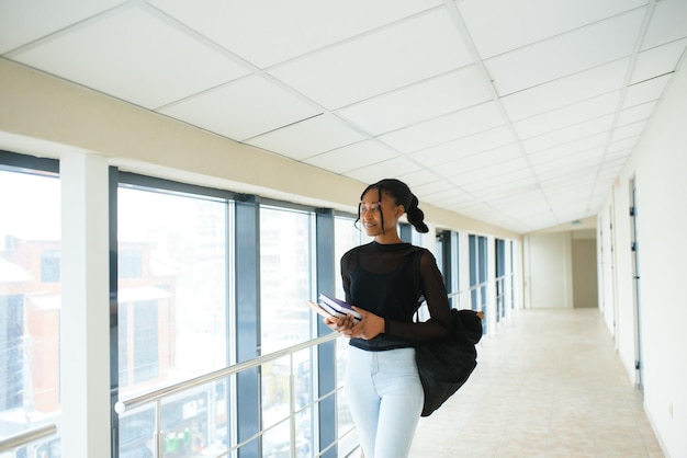 Jolie étudiante afro-américaine avec sac à dos et paperasse dans la salle de classe de l'université