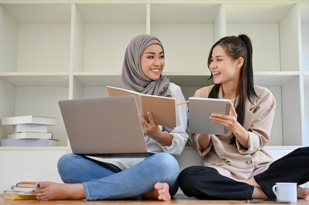 Jolie étudiante asiatique à la bibliothèque avec son amie musulmane discutant du projet