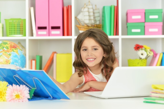 Jolie étudiante avec livre, globe et ordinateur portable en classe