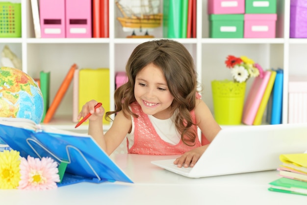 Jolie étudiante avec livre, globe et ordinateur portable en classe