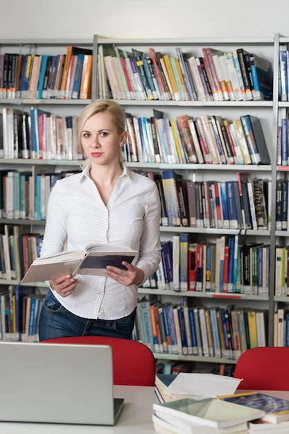 Jolie étudiante avec des livres travaillant dans une bibliothèque de lycée