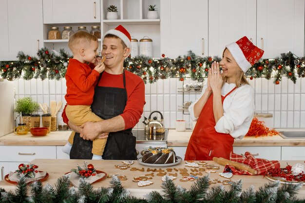 Une jolie famille joyeuse à la maison riant et s'amusant dans la cuisine Un petit fils mignon taquine son père avec du bisquit et sa mère rit en les regardant