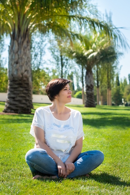 Jolie femme adulte est assise sur l'herbe sous les palmiers. concept de citoyen âgé de retraite actif et heureux à l'extérieur. aime les vacances et les voyages