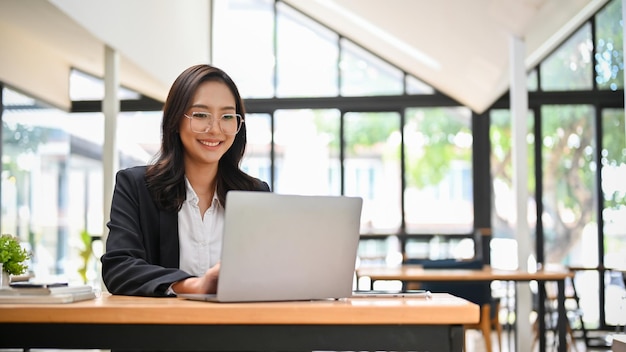 Jolie femme d'affaires asiatique travaillant sur son projet sur ordinateur portable dans un espace de coworking de café