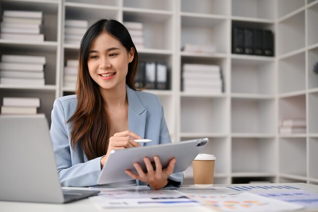 Jolie femme d'affaires asiatique utilisant sa tablette et son ordinateur portable à son bureau