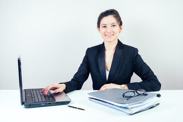 Jolie femme d'affaires brune dans un costume d'affaires élégant travaillant au bureau avec un concept d'ordinateur portable d'affaires et d'économie