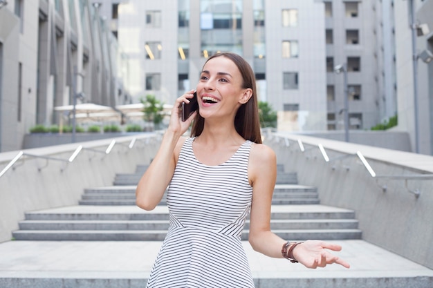 Jolie femme d'affaires brune heureuse parle sur son smartphone et regarde ailleurs.